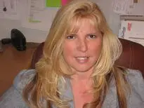 A woman with long blonde hair sitting in front of a wall.